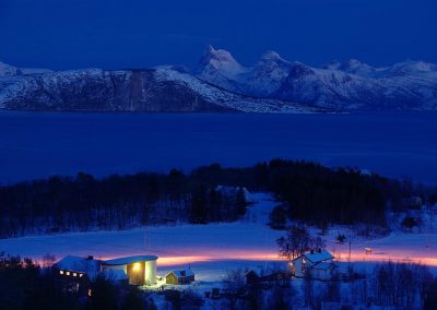 Stetind og Skarberget i Tysfjord i blåtimen med fjord og snøkledd fjell og gård i forgrunn